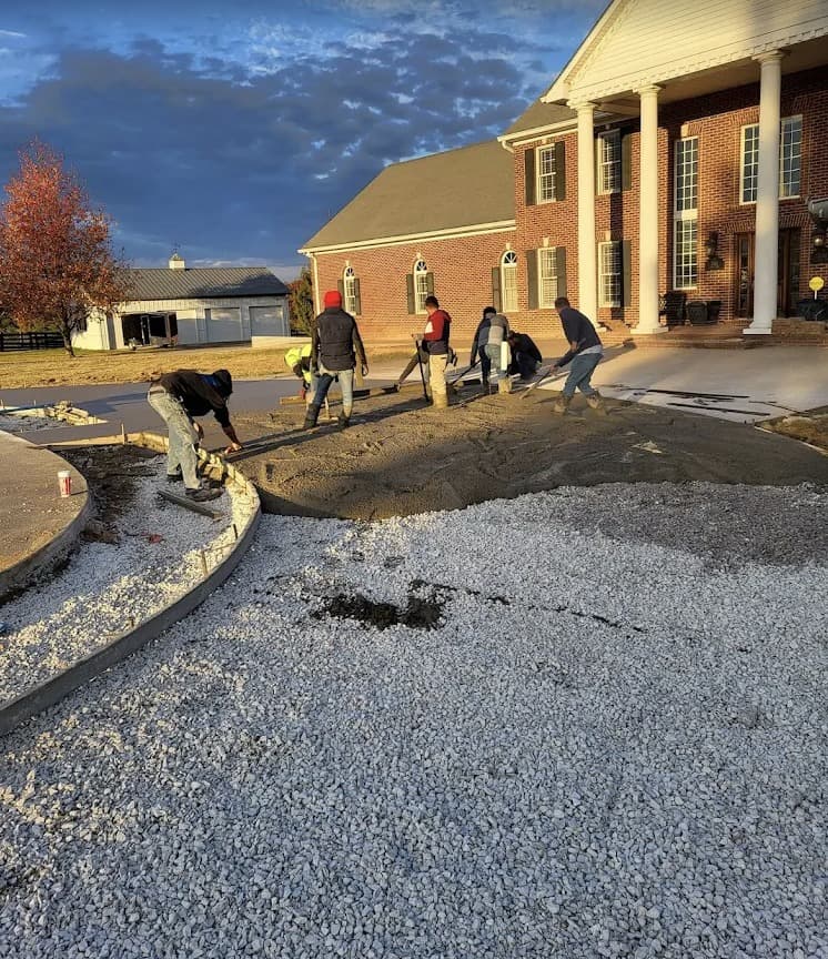 Crew pouring curved concrete driveway at brick home at dusk in Dallas